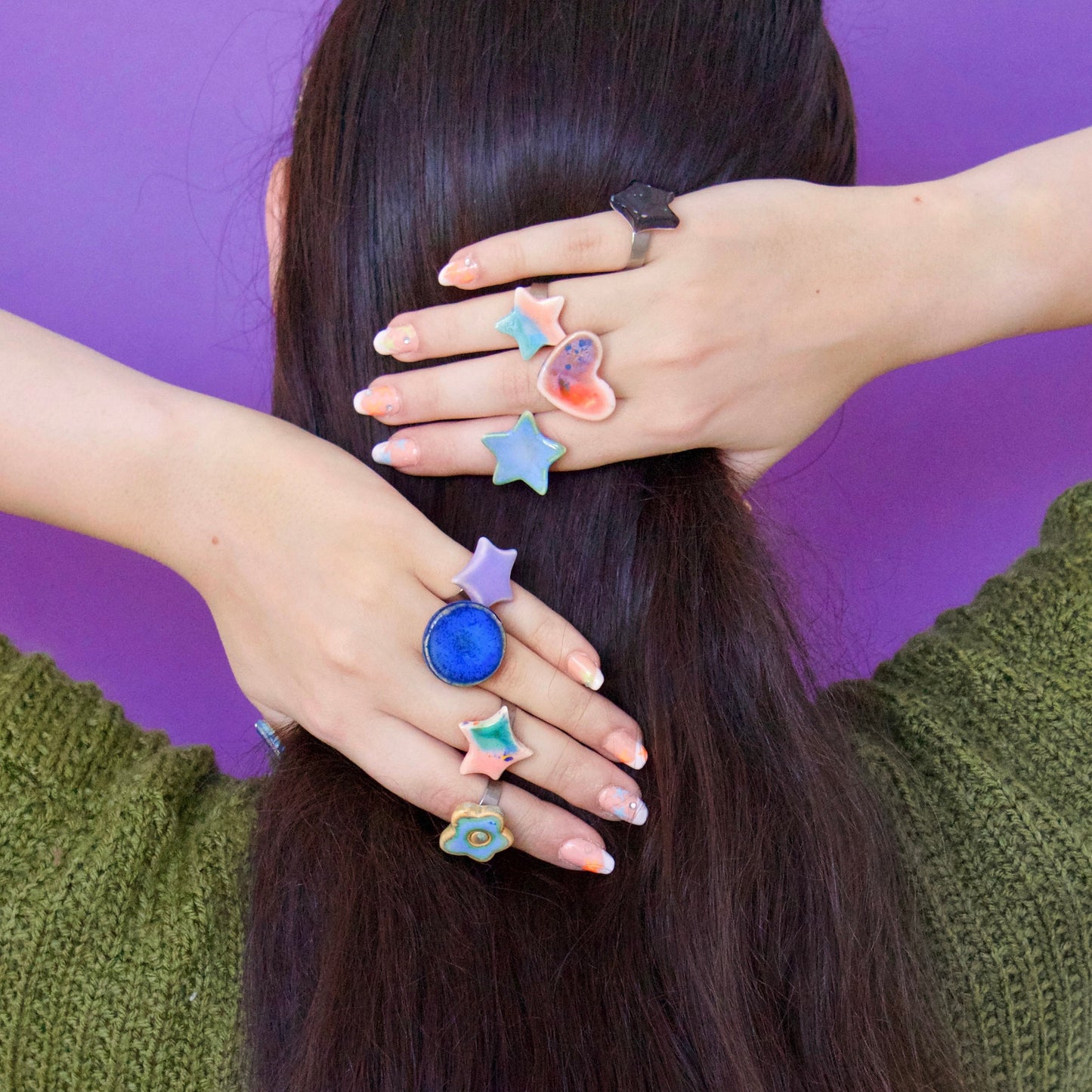 Mâini decorate cu inele handmade din ceramică în forme variate (stea, inimă, floare, cerc), glazurate în nuanțe pastel și montate pe tije din oțel inoxidabil – bijuterii Ecluze Studio.