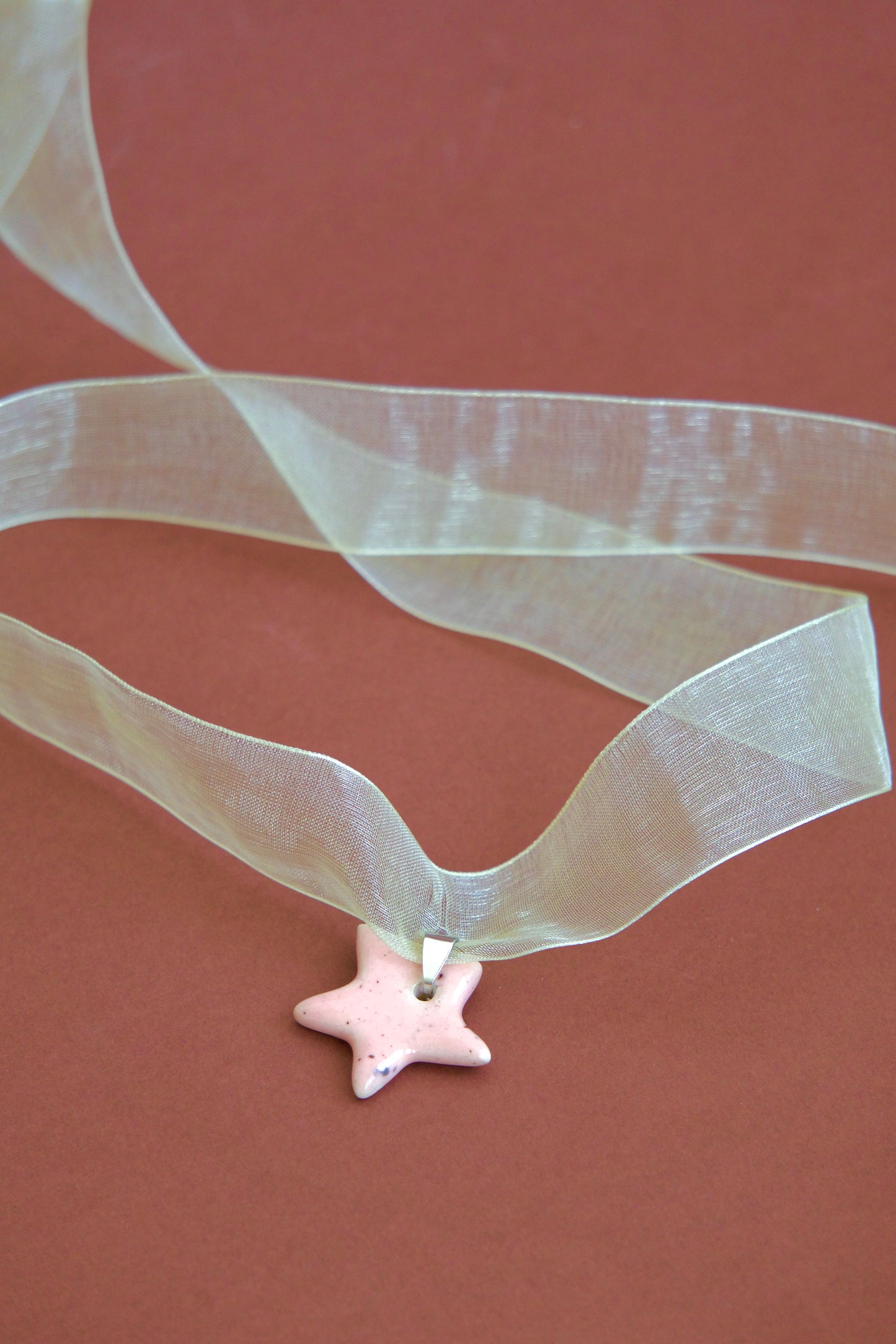 Colier unicat cu pandantiv stea roz-pastel din ceramica pe snur din organza galben deschis pe fundal maro.