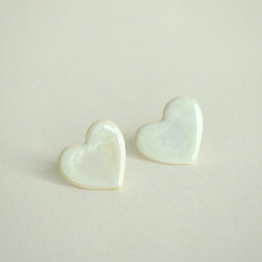 Cercei handmade din porțelan în formă de inimă, alb perlat,finisaj lucios pe fundal crem.