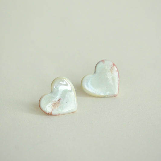 Cercei handmade din porțelan în formă de inimă, alb perlat cu accente roz pe fundal alb crem.
