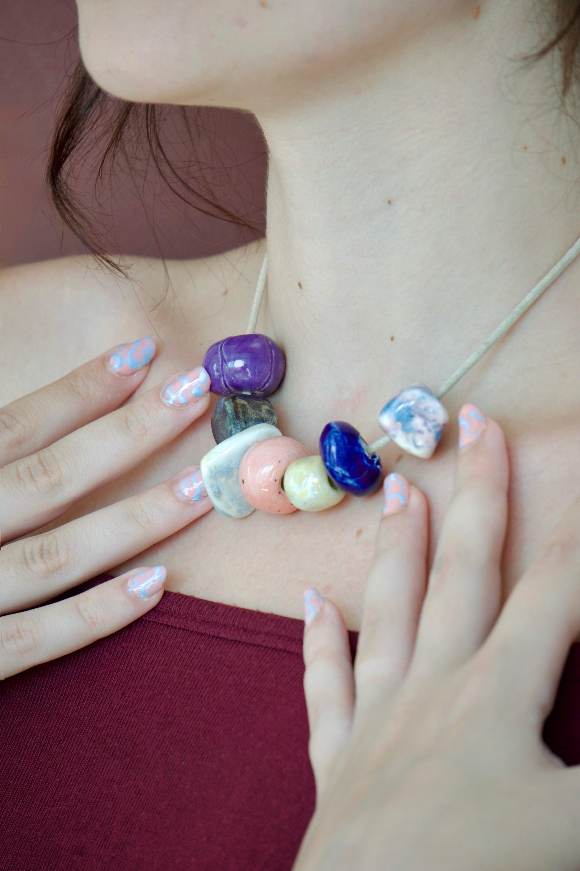 Colier unicat cu charmuri realizate manual din ceramica de diferite culori (albastru, alb, mov, oranj, ocur, negru) pe snur bej din suede purtat la gat.