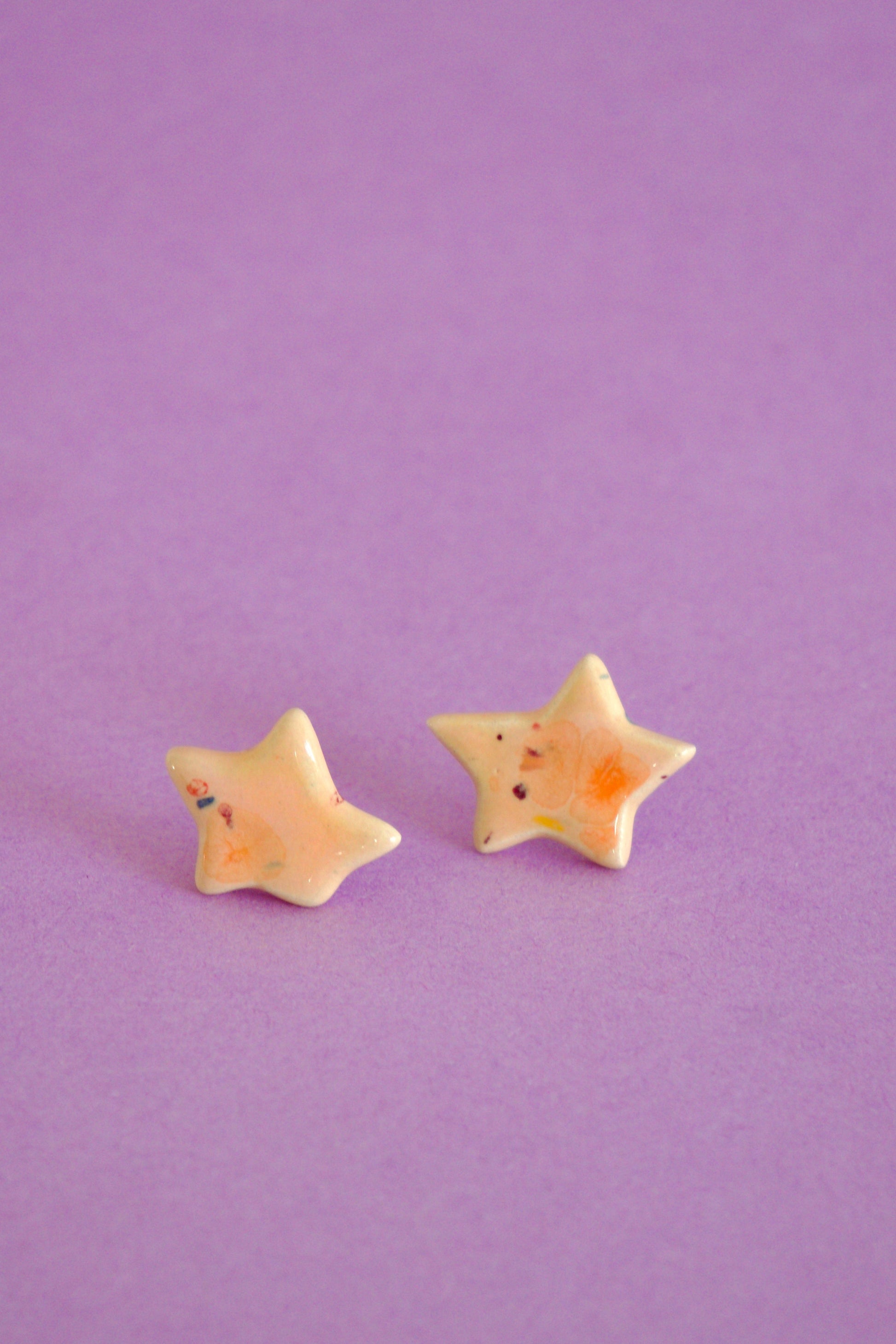 Cercei handmade din ceramică în formă de steluță Coral & Rosé, cu glazuri lucioase și tije hipoalergenice pe fundal mov deschis.