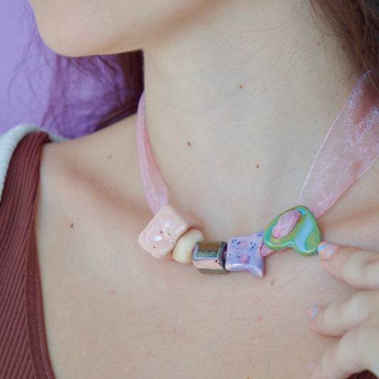 Colier unicat cu 5 charmuri colorate din ceramica de diferite culori (verde, mov, roz, bej, negru) pe snur roz din organza purtat la gat impreuna cu cercei inimioare roz si mov.