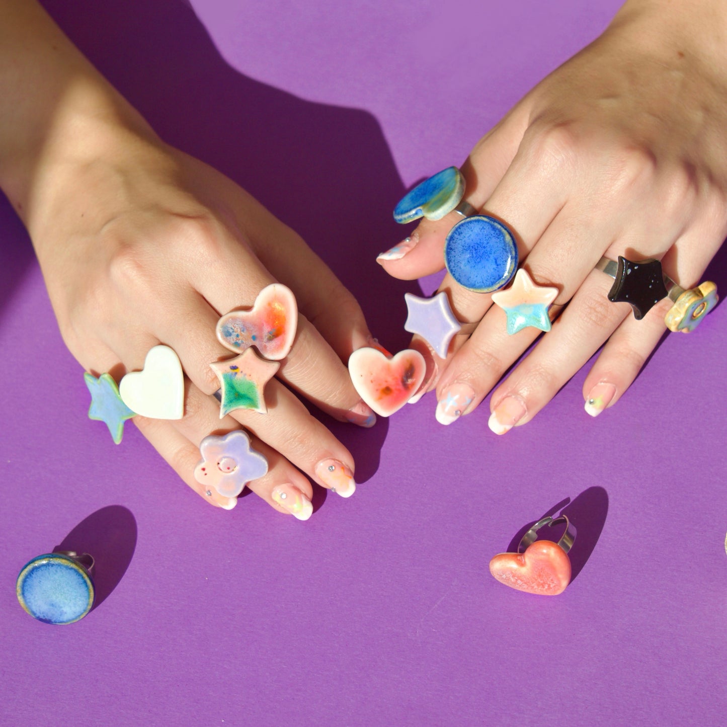 Inele handmade din porțelan în forme de inimă și stea, cu glazură colorată, purtate pe mai multe degete, bijuterii artizanale unicat.