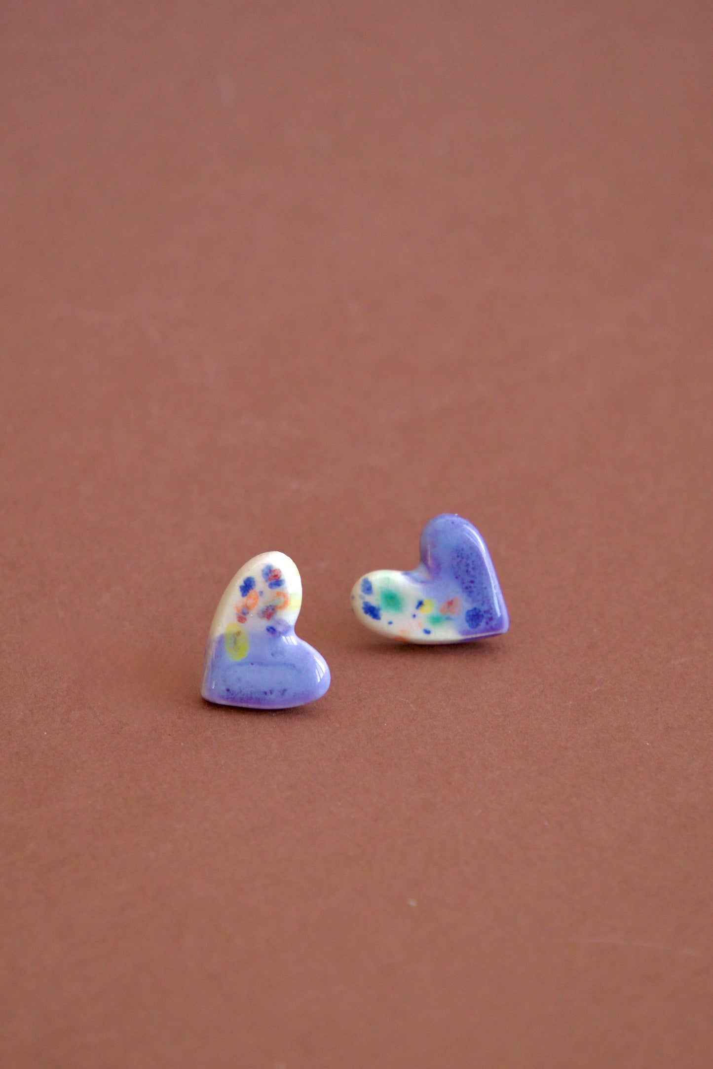 Cercei handmade din ceramică asimetrici – inimi lila și lucioase, cu tije hipoalergenice.