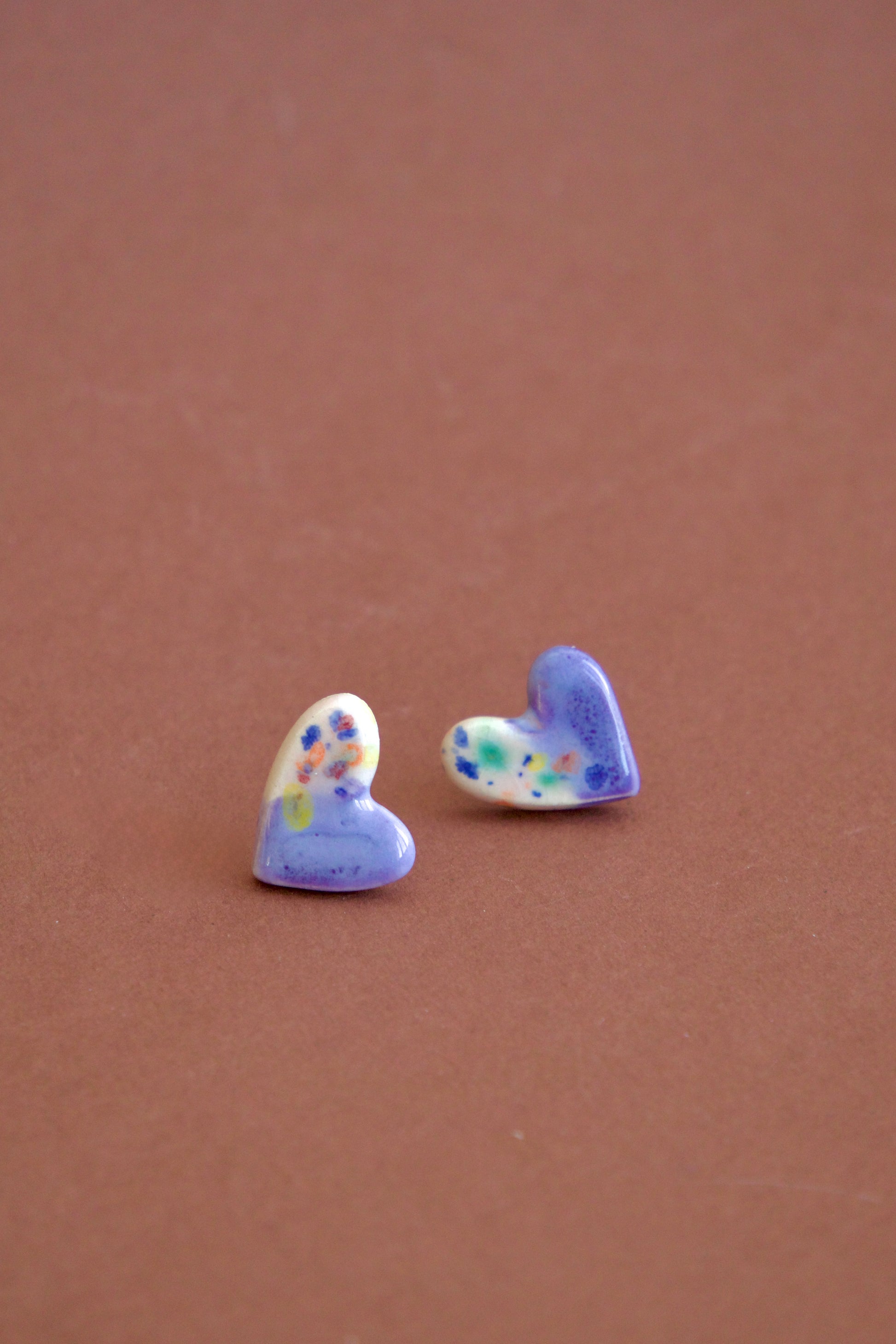Cercei handmade din ceramică asimetrici – inimi lila și lucioase, cu tije hipoalergenice.