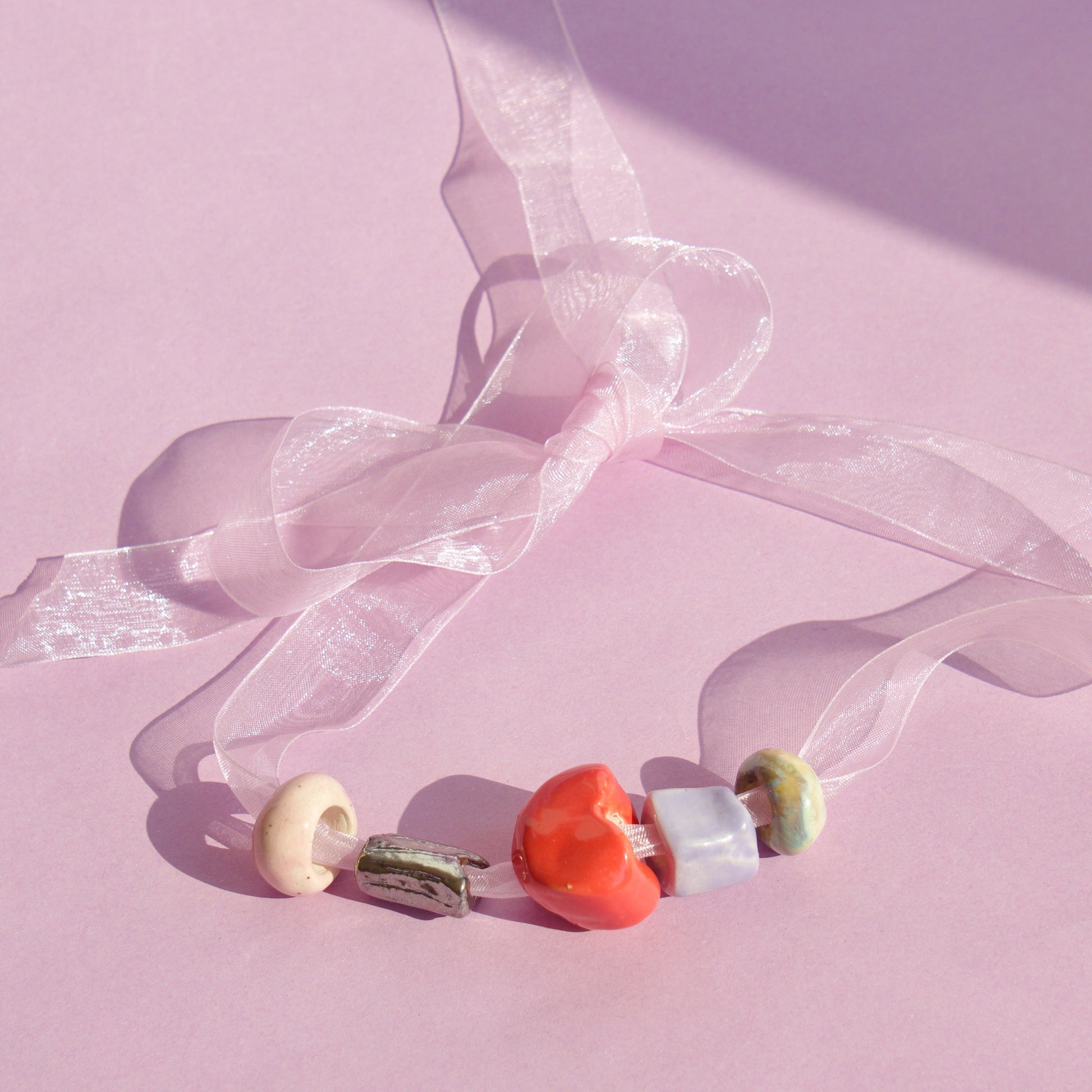 Colier cu margele din ceramica confectionate manual pe snur din organza pe fundal roz.