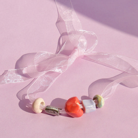 Colier cu margele din ceramica confectionate manual pe snur din organza pe fundal roz.