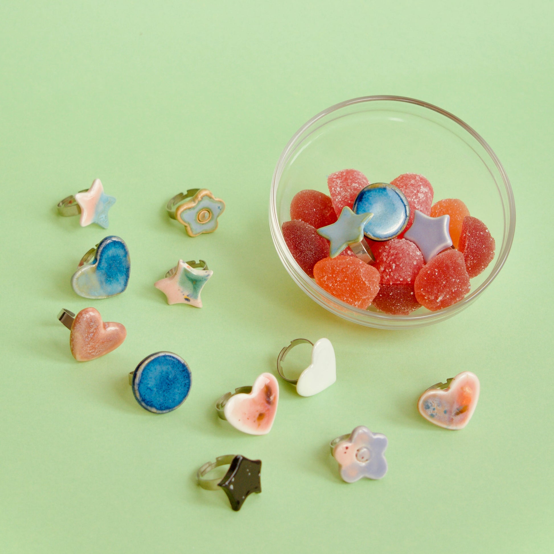 Inele handmade din porțelan, inimă cu glazură artistică multicoloră, fotografiate pe fundal verde – bijuterii artizanale unicat.