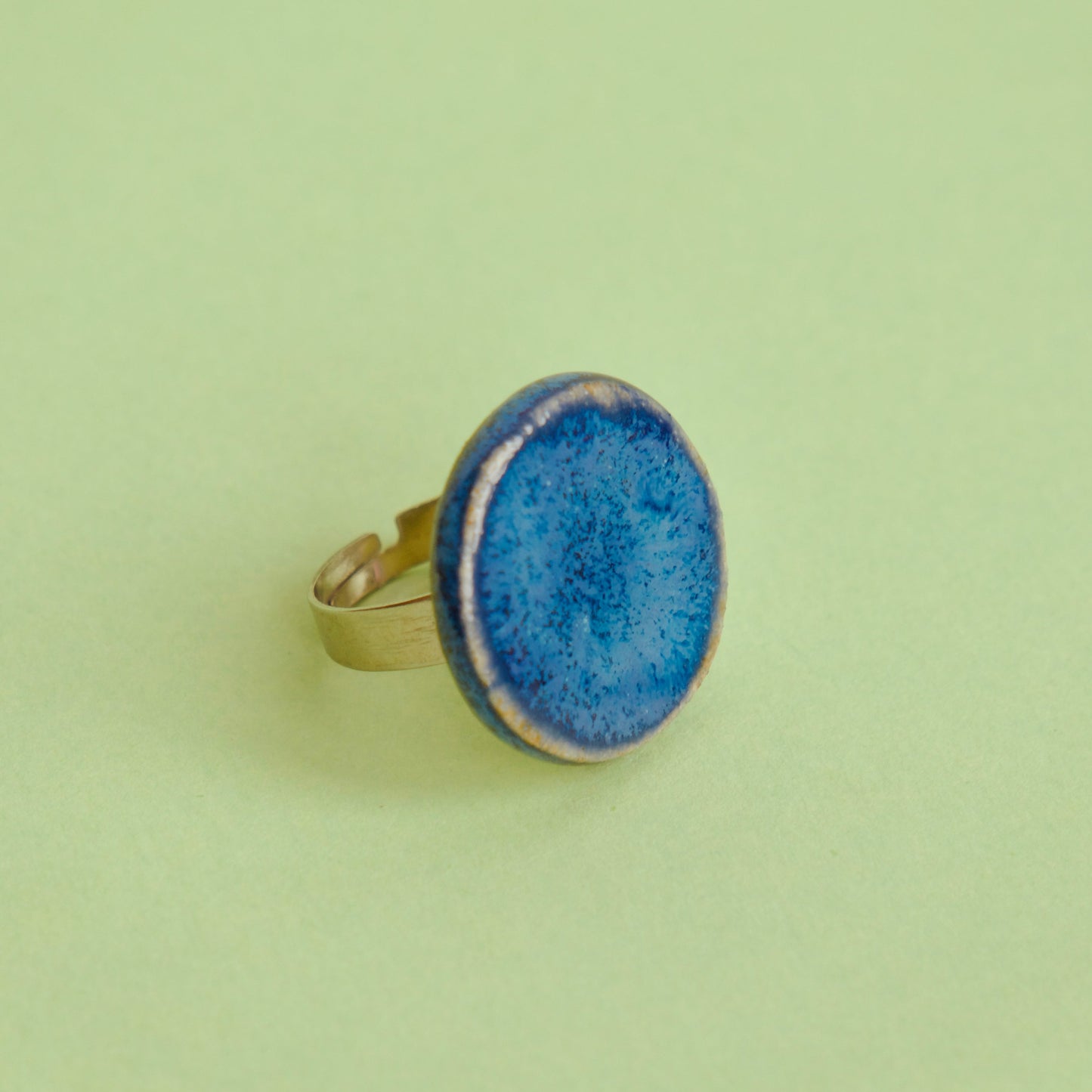 Inel handmade din ceramică cu glazură albastru intens, montat pe suport reglabil din oțel inoxidabil, pe fundal verde – bijuterie Ecluze Studio.