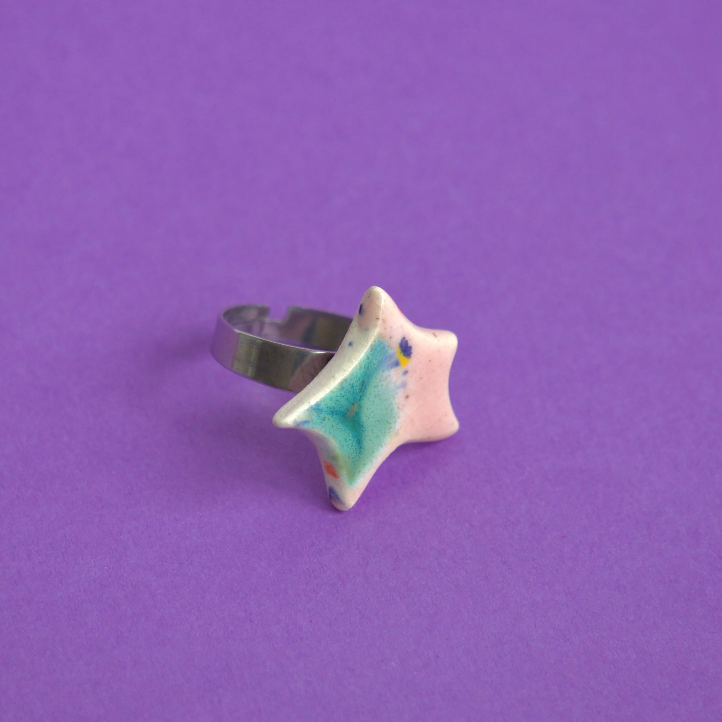 Inel din ceramică cu formă de stea, glazură roz și verde, montat pe suport reglabil, pe fundal mov – bijuterie Ecluze Studio.