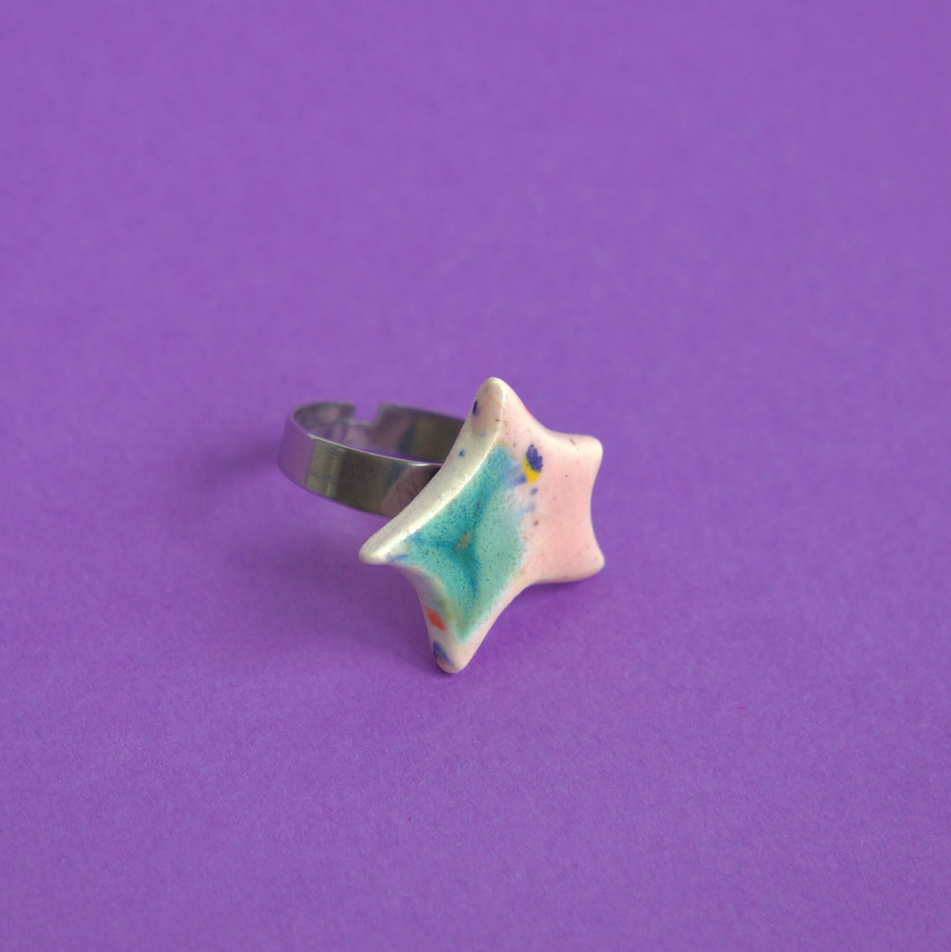Inel din ceramică cu formă de stea, glazură roz și verde, montat pe suport reglabil, pe fundal mov – bijuterie Ecluze Studio.