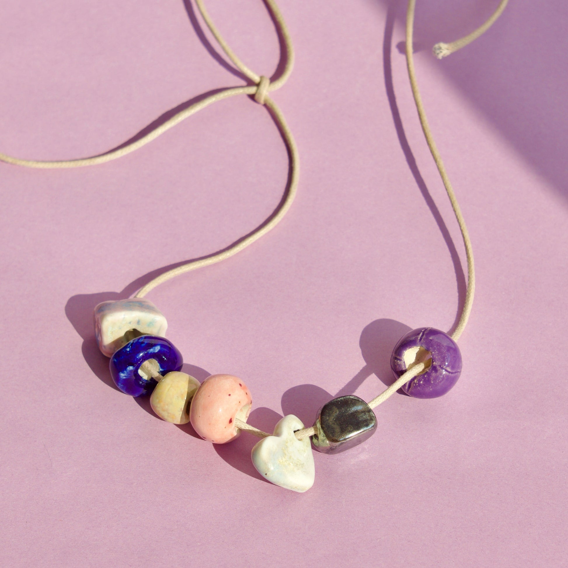Colier unicat cu charmuri realizate manual din ceramica de diferite culori (albastru, alb, mov, oranj, ocur, negru) pe snur bej din suede.