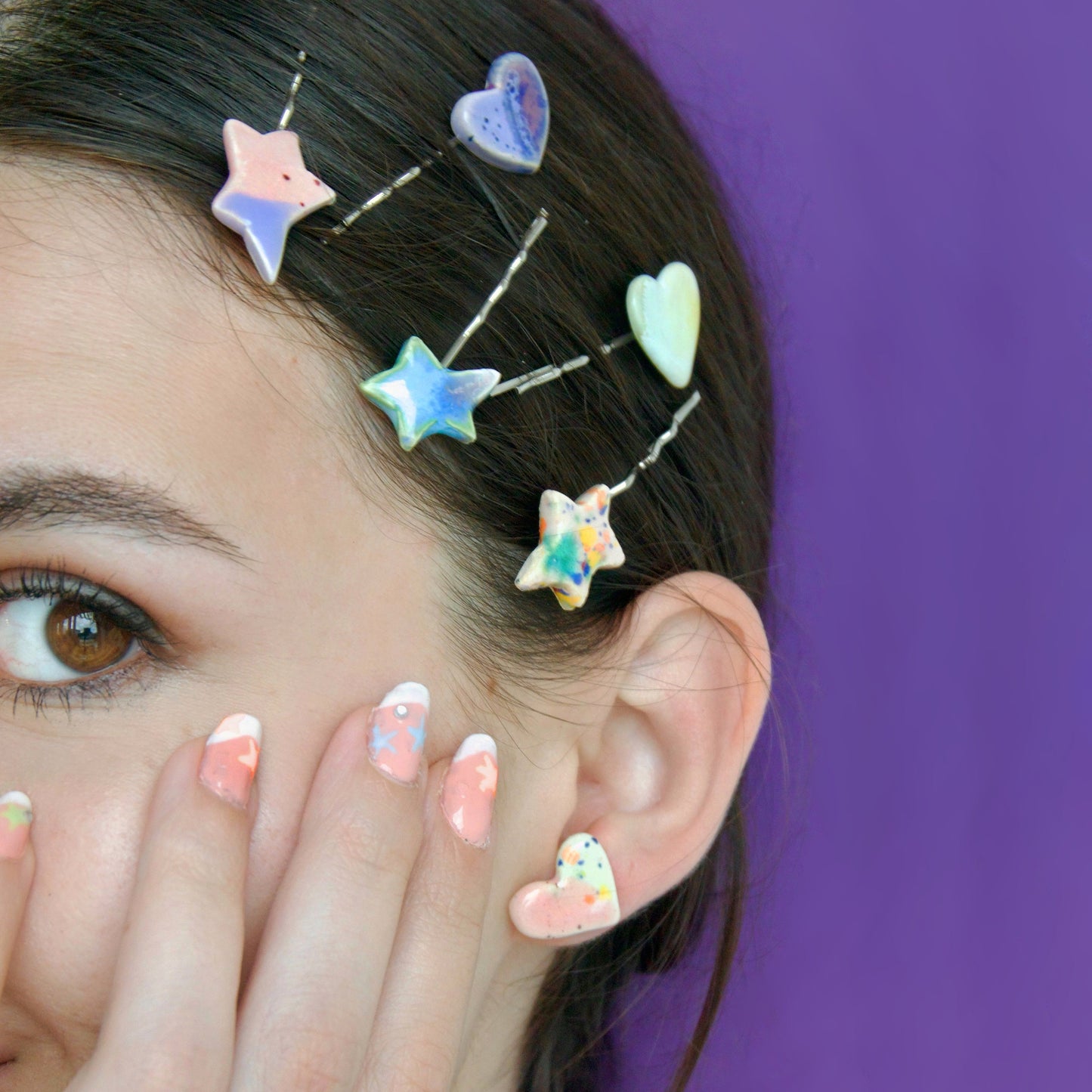 Agrafe de păr decorate cu forme ceramice handmade (inimă și stea) în nuanțe pastel, alături de un cercel ceramic cu glazură colorată – bijuterii Ecluze Studio.