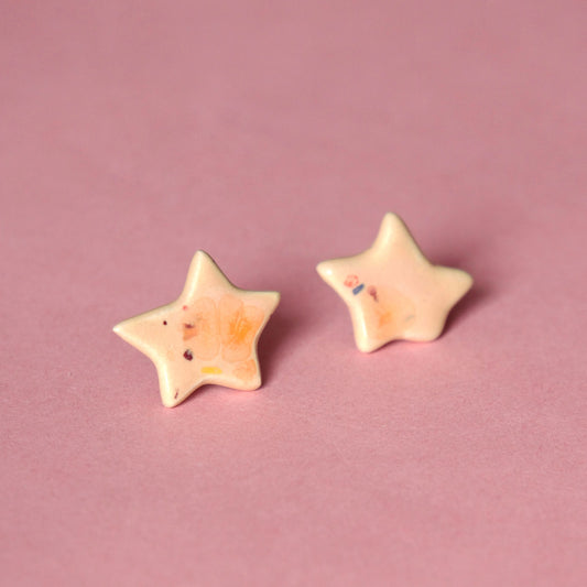 Cercei handmade din ceramică în formă de steluță culori Coral & Rosé, cu glazuri lucioase și tije hipoalergenice pe fundal roz.