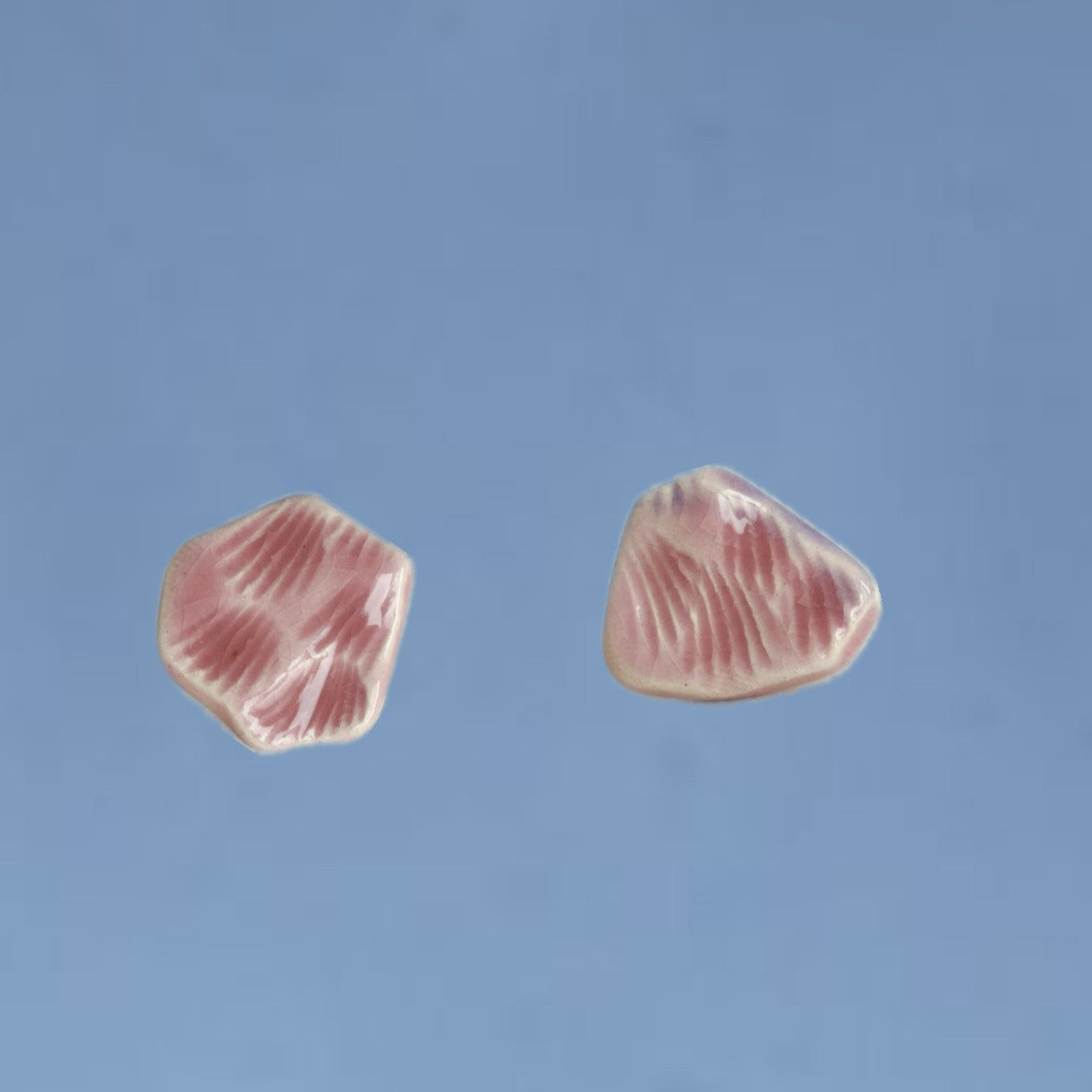 Cercei handmade din porțelan cu formă organică, roz pastel pe fundal albastru.