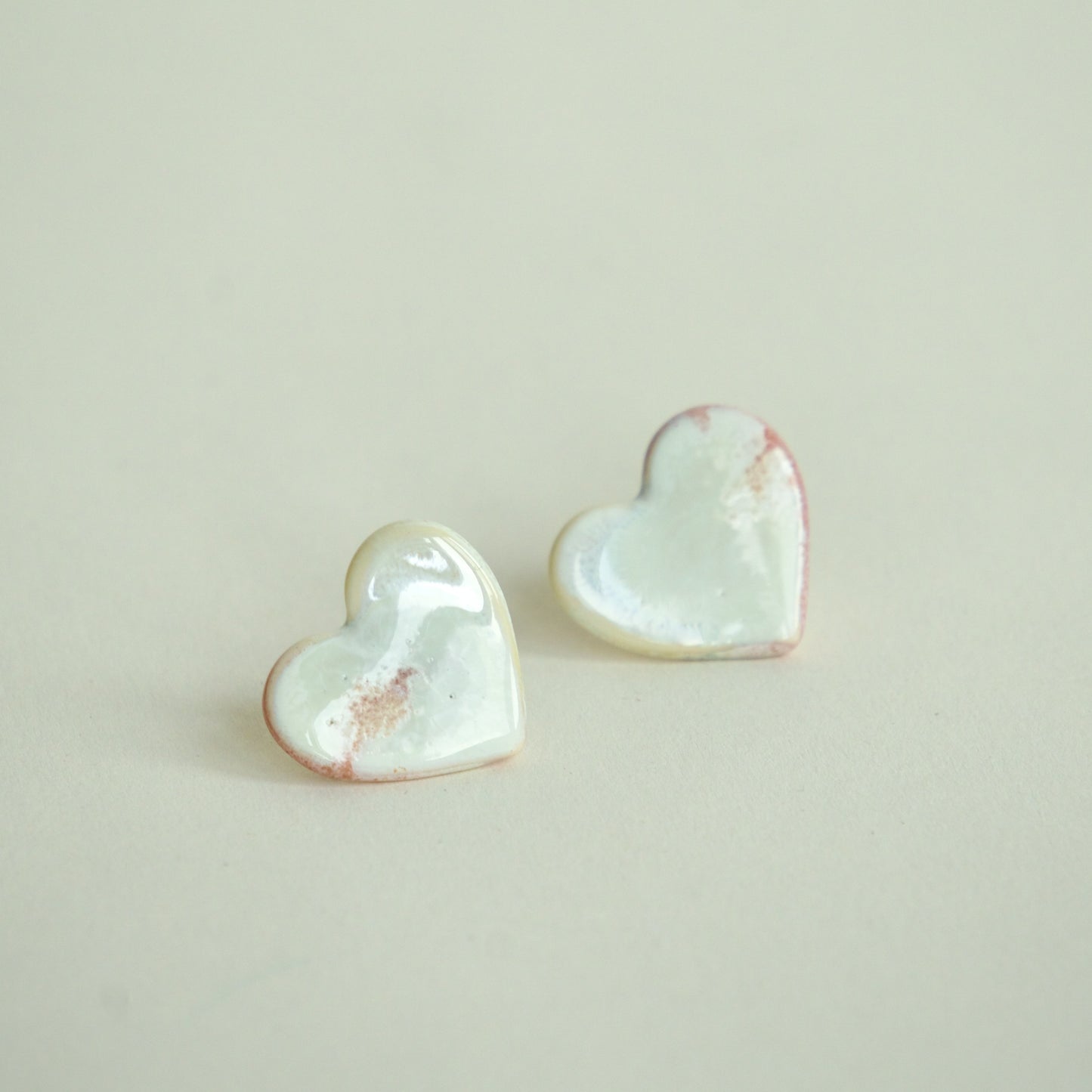 Cercei handmade din porțelan în formă de inimă, alb perlat cu accente roz pe fundal alb crem.