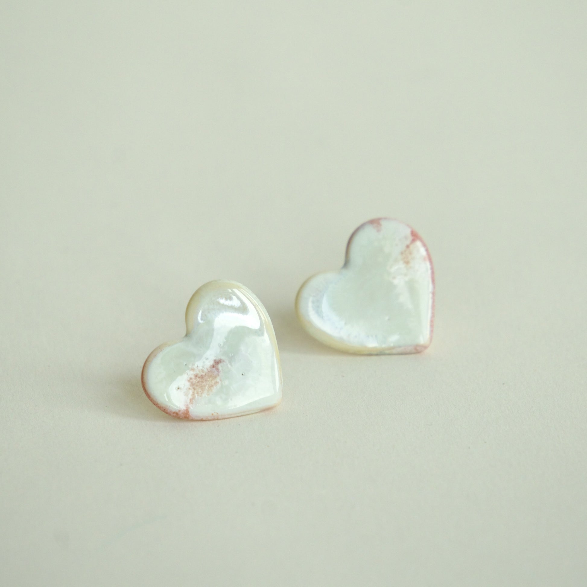 Cercei handmade din porțelan în formă de inimă, alb perlat cu accente roz pe fundal alb crem.