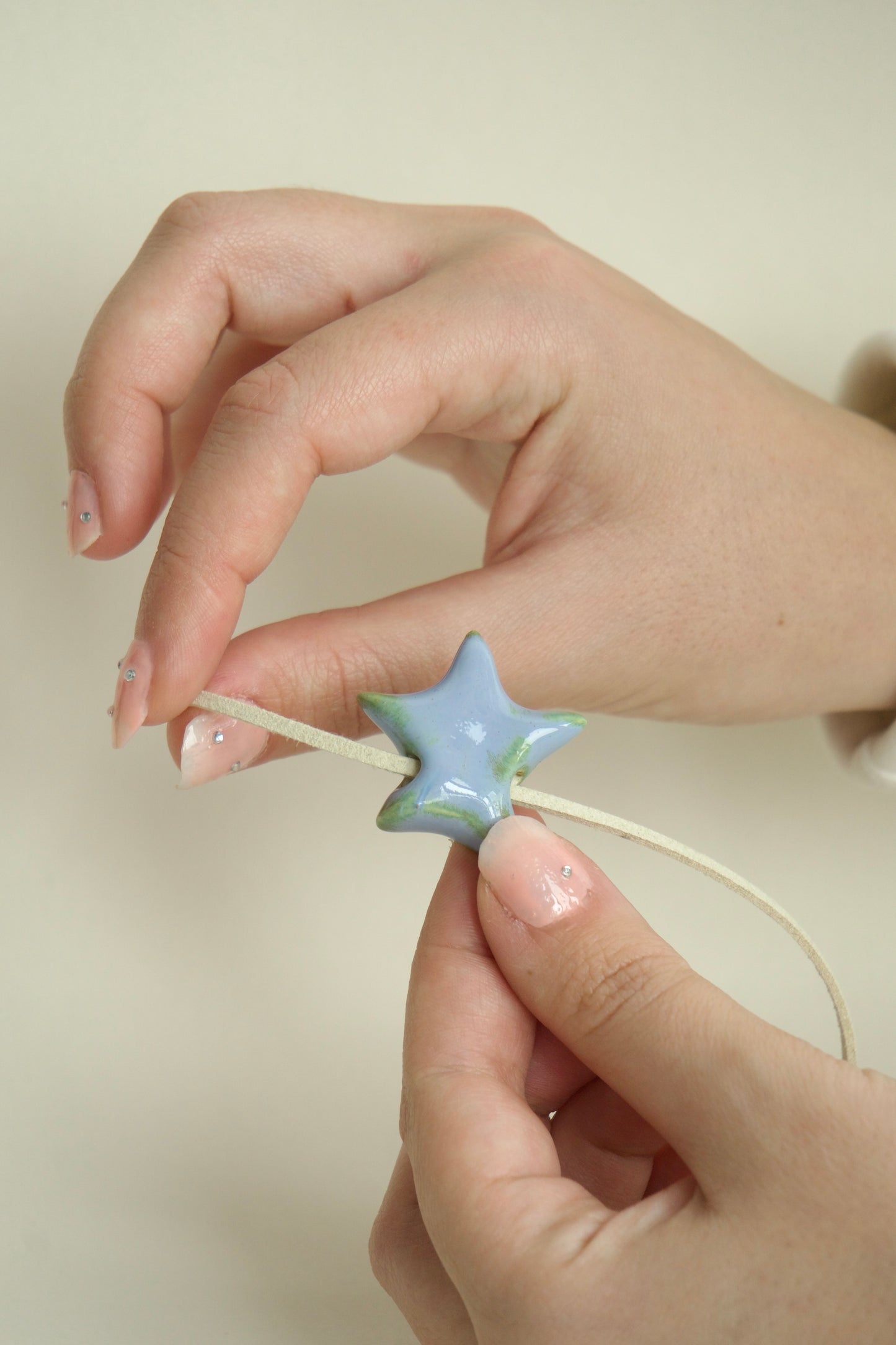 Charm handmade din ceramică în formă de stea albastru verzui, cu șnur suede bej, ținut în mână, ideal pentru coliere personalizate.