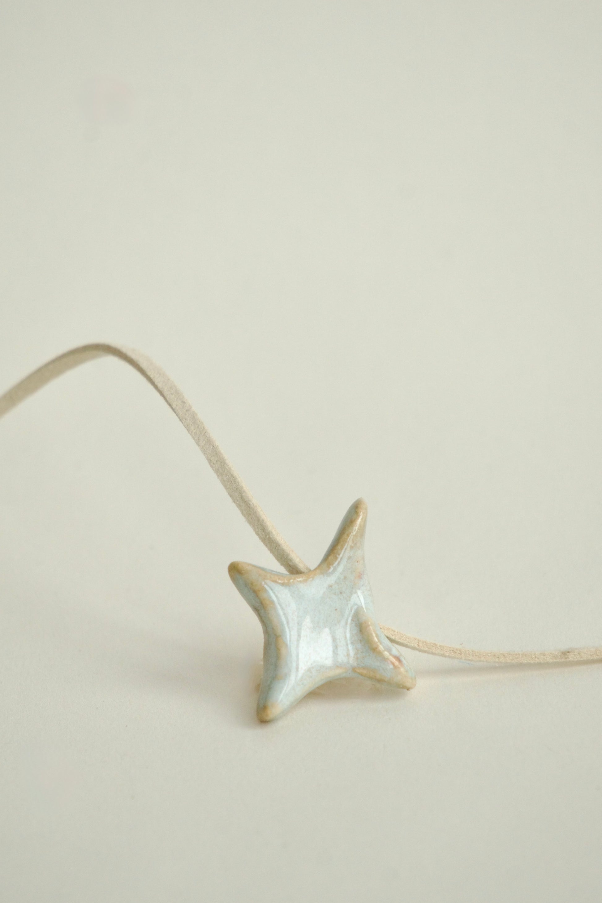 Charm handmade din ceramică în formă de stea alb perlat, cu șnur suede bej, ideal pentru coliere personalizate.