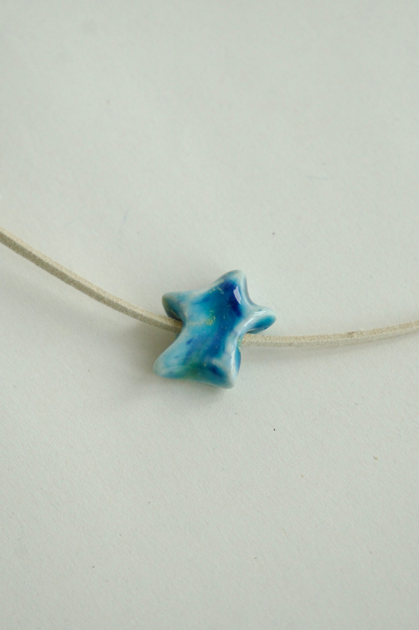 Charm ceramic albastru în formă de stea, pe un șnur simplu, fotografiat pe fundal alb.