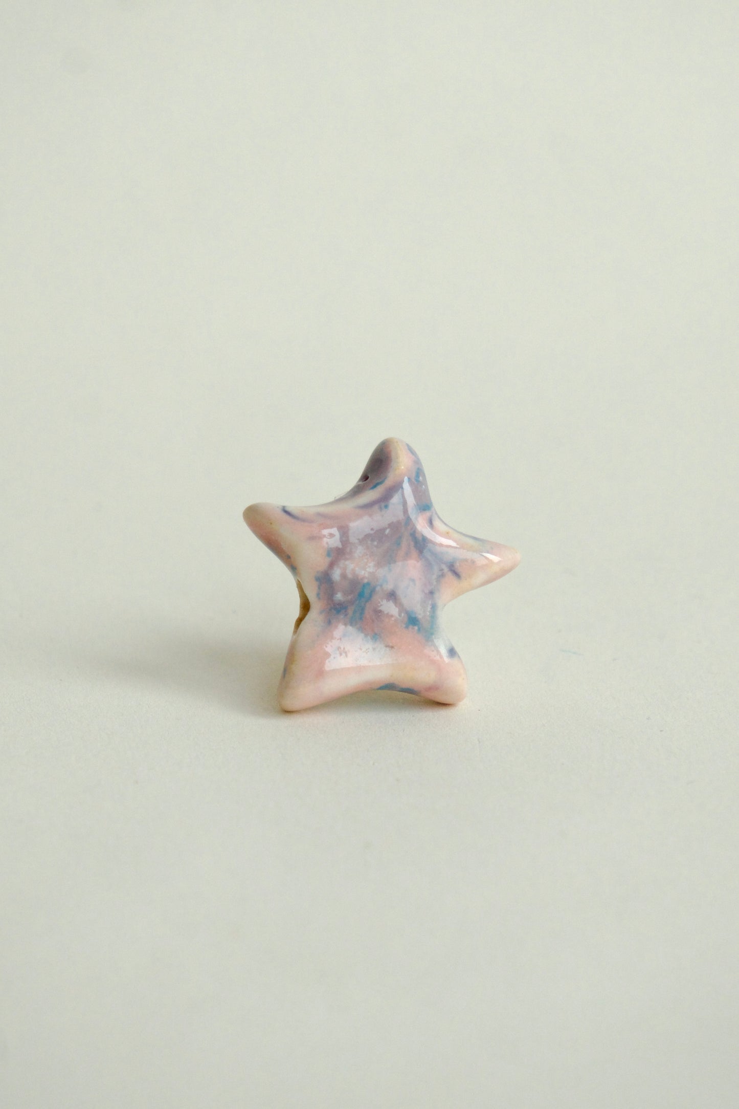 Charm handmade în formă de steluță din ceramică, roz pastel cu accente albastre, finisaj lucios, design unicat.