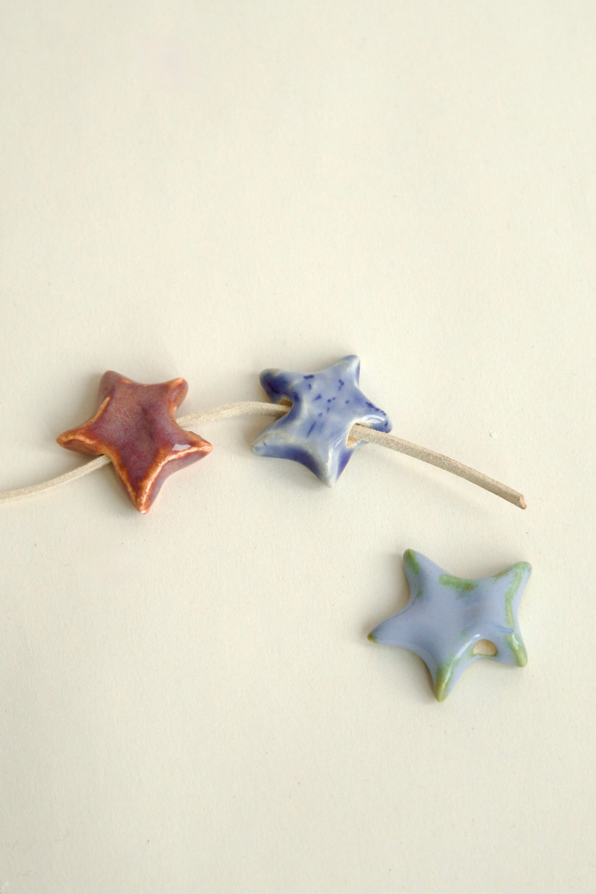 Trei charmuri din ceramică în formă de stea cu șnur suede bej, ideale pentru a fi accesorizate pe un colier personalizat.