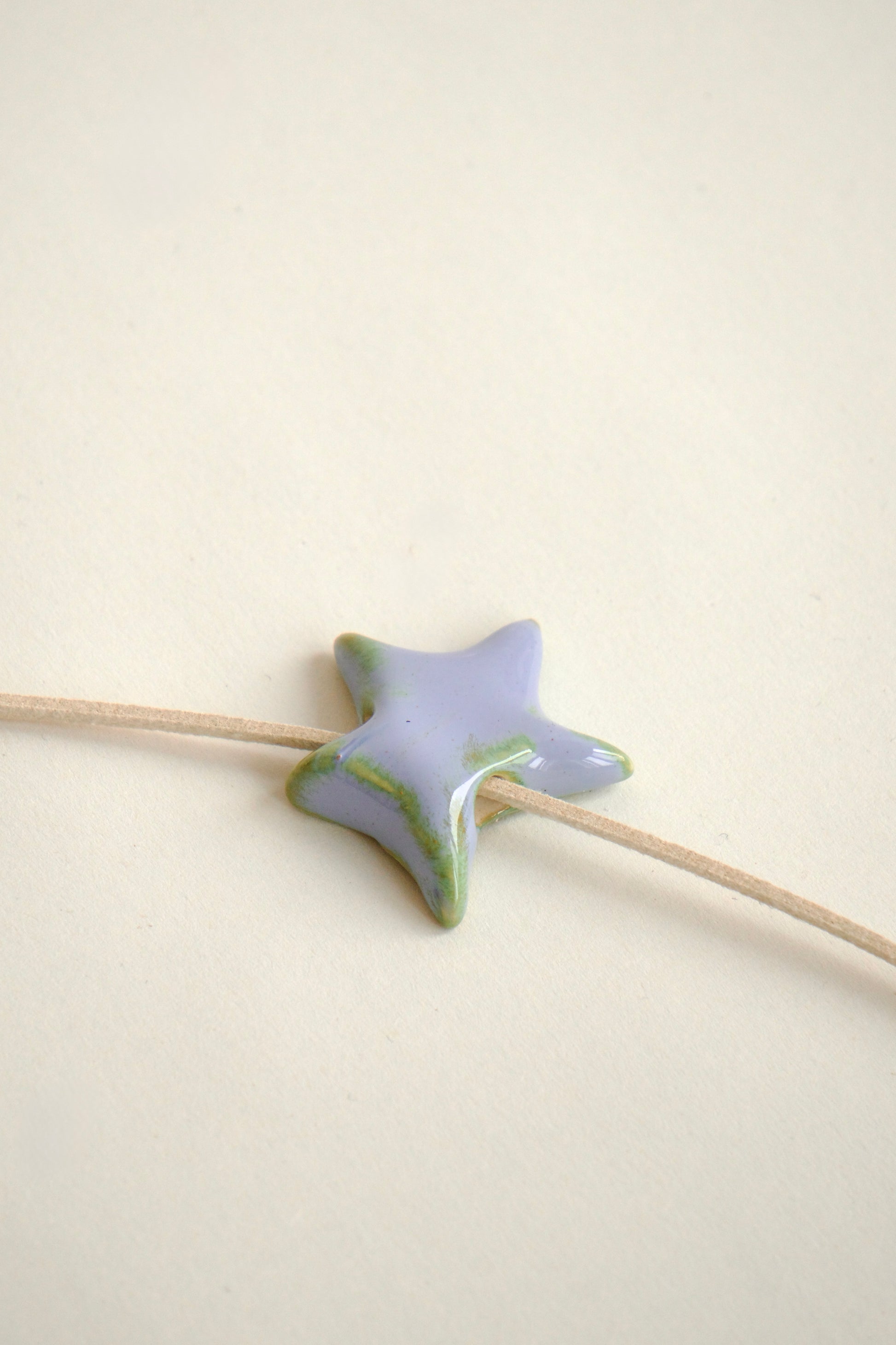 Charm handmade din ceramică în formă de stea lila cu accente verzi, cu șnur suede bej, ideal pentru coliere personalizate.