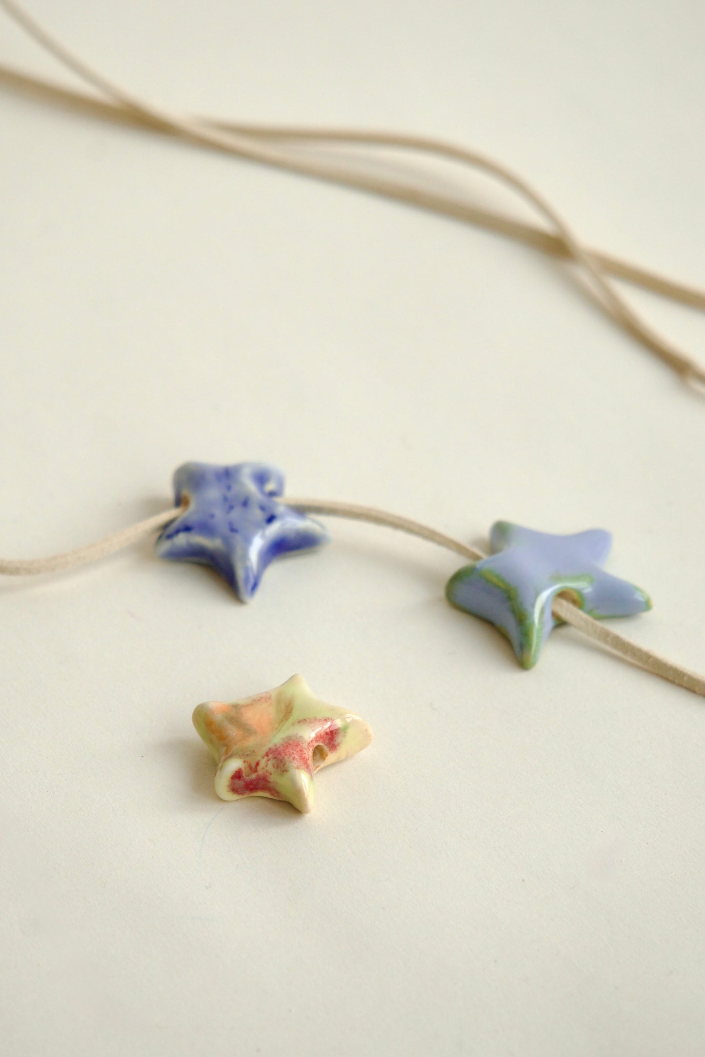 Set de charmuri ceramice handmade în formă de stea, culori variate (albastru, bleu, roșu, galben), pentru coliere personalizate și bijuterii unicat.
