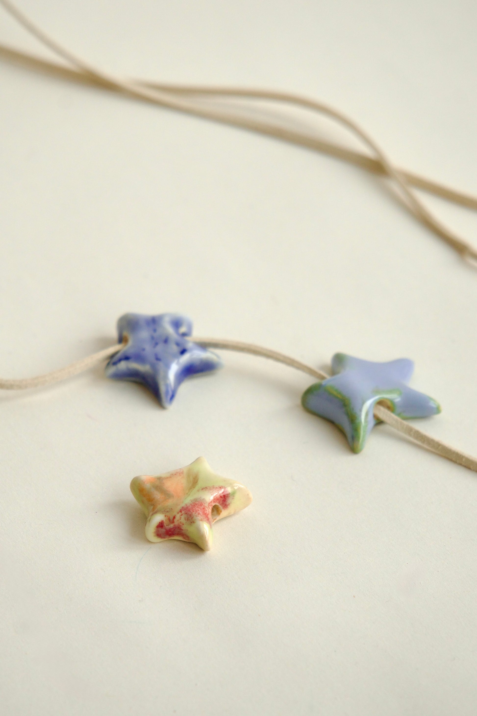 Set de charmuri ceramice handmade în formă de stea, culori variate (albastru, bleu, roșu, galben), pentru coliere personalizate și bijuterii unicat.