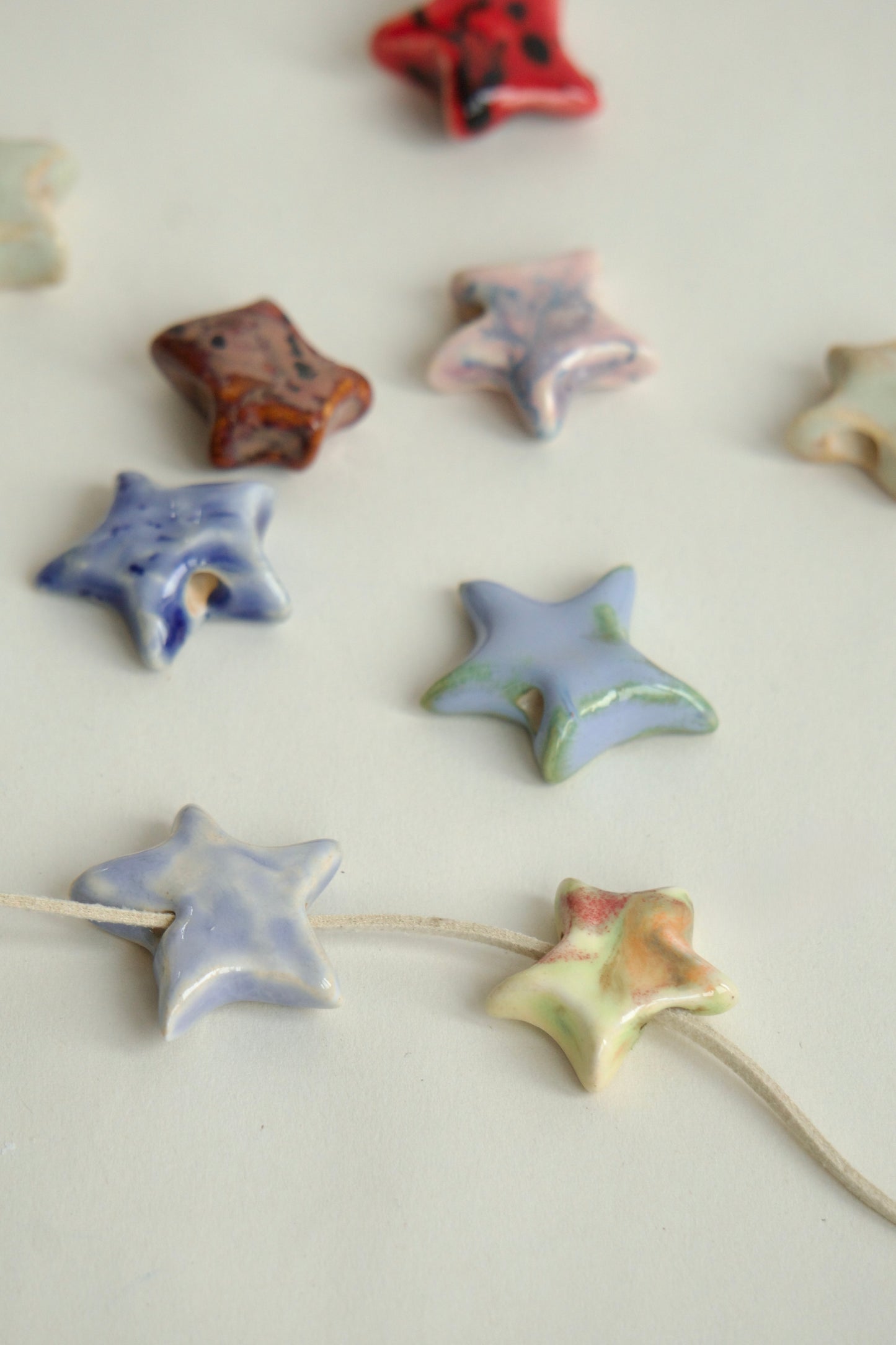 Set de charmuri handmade din ceramică, forme de steluțe în culori variate – pastel, roșu, albastru, verde – ideale pentru coliere personalizate.
