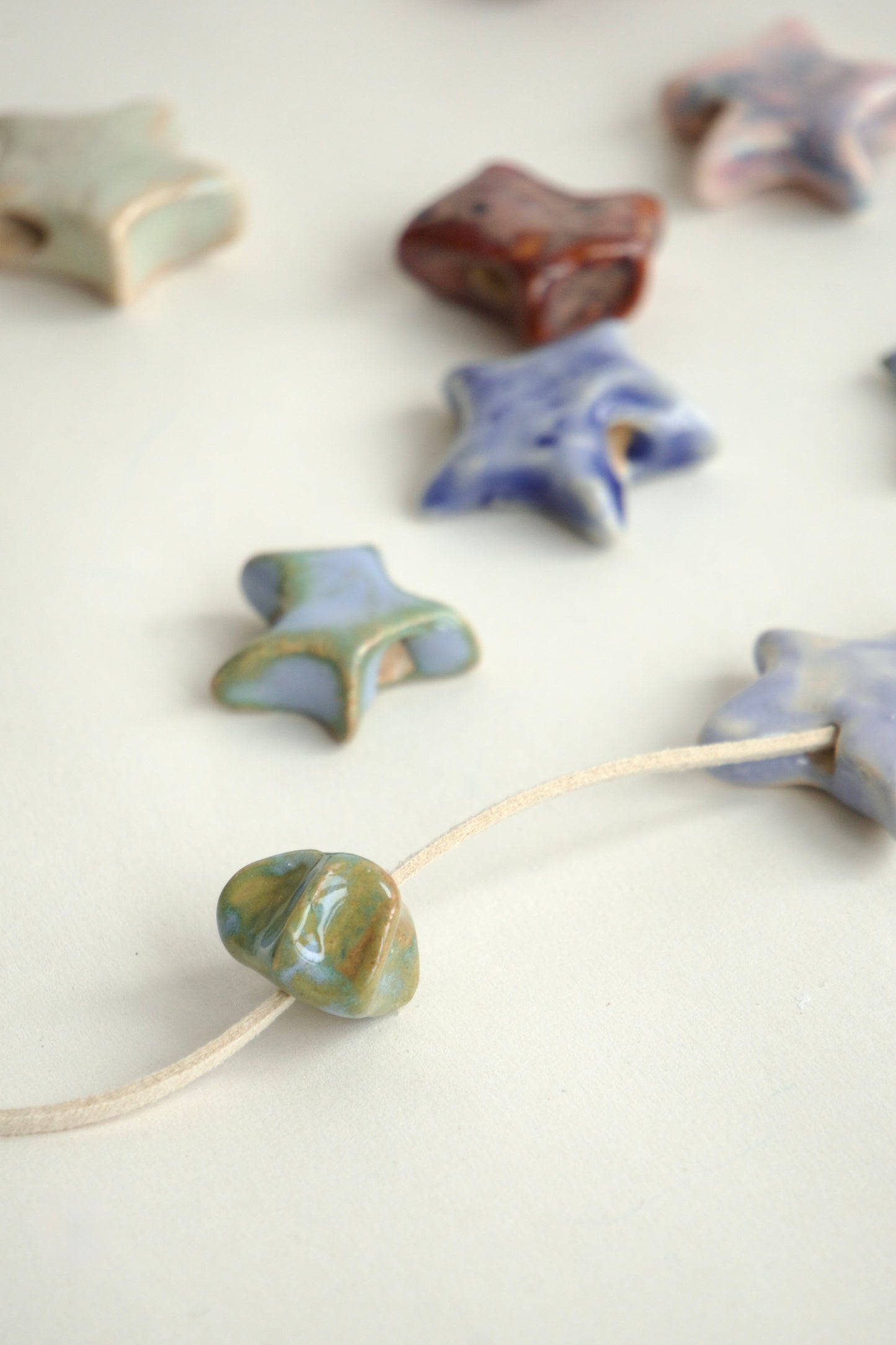 Charm handmade din ceramică în formă de stea albastru cu accente verzi, cu șnur suede bej, ideal pentru coliere personalizate.