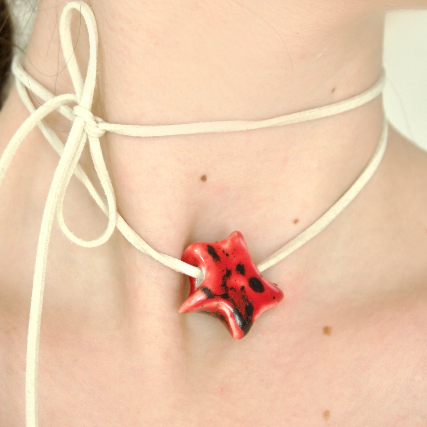 Colier cu pandantiv stea rosu din ceramica prins pe snur suede bej purtat la gat - bijuterii ecluze studio.