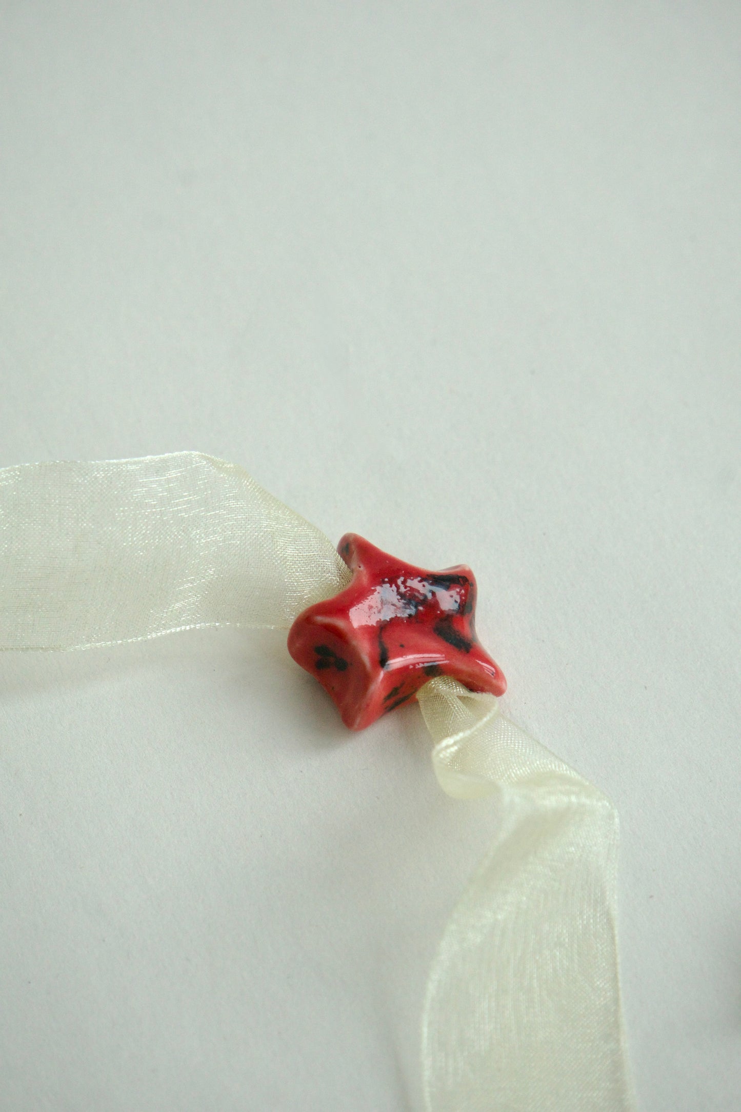 Charm din ceramica în formă de stea, rosu cu accente negre.