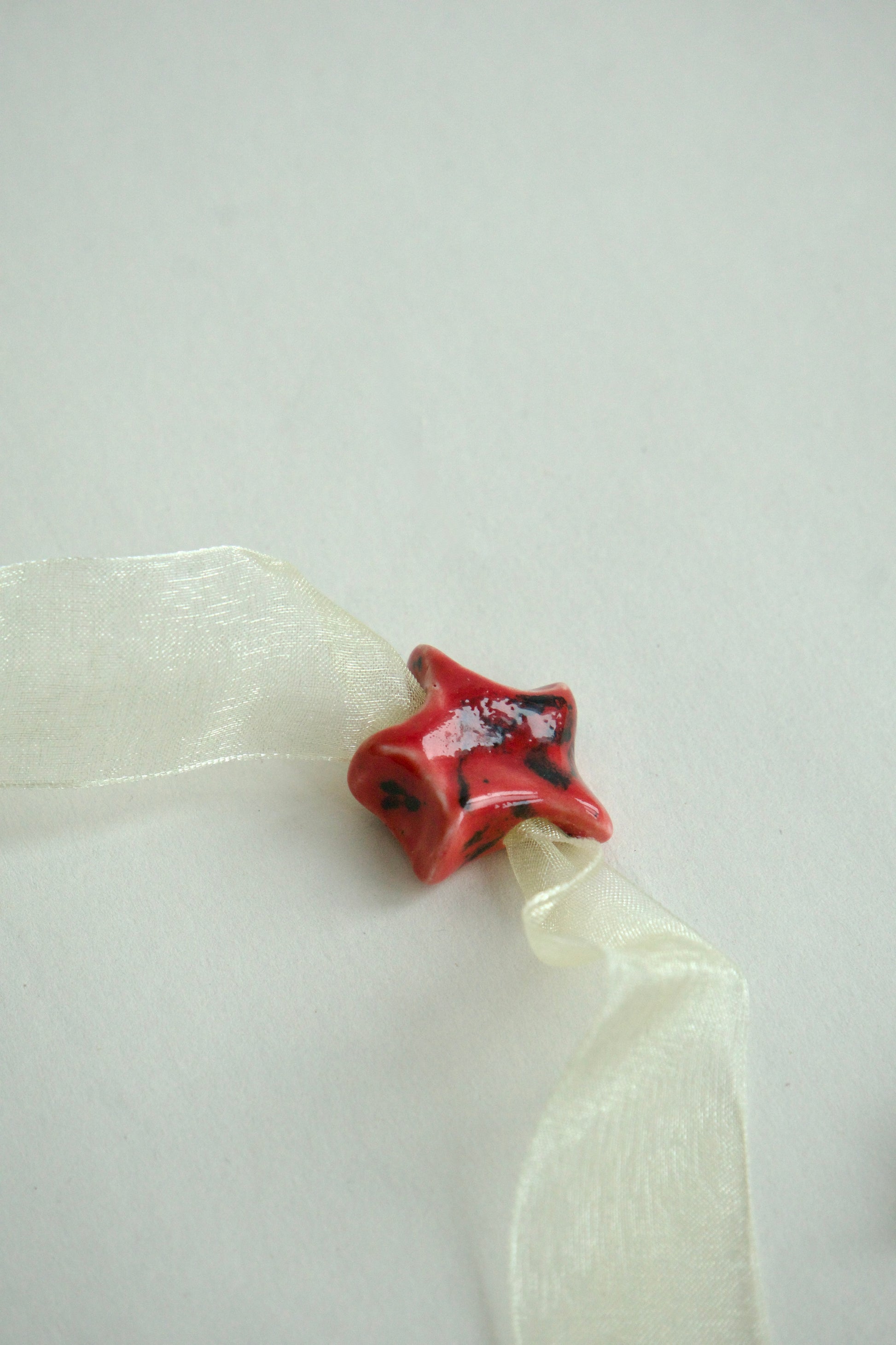 Charm din ceramica în formă de stea, rosu cu accente negre.