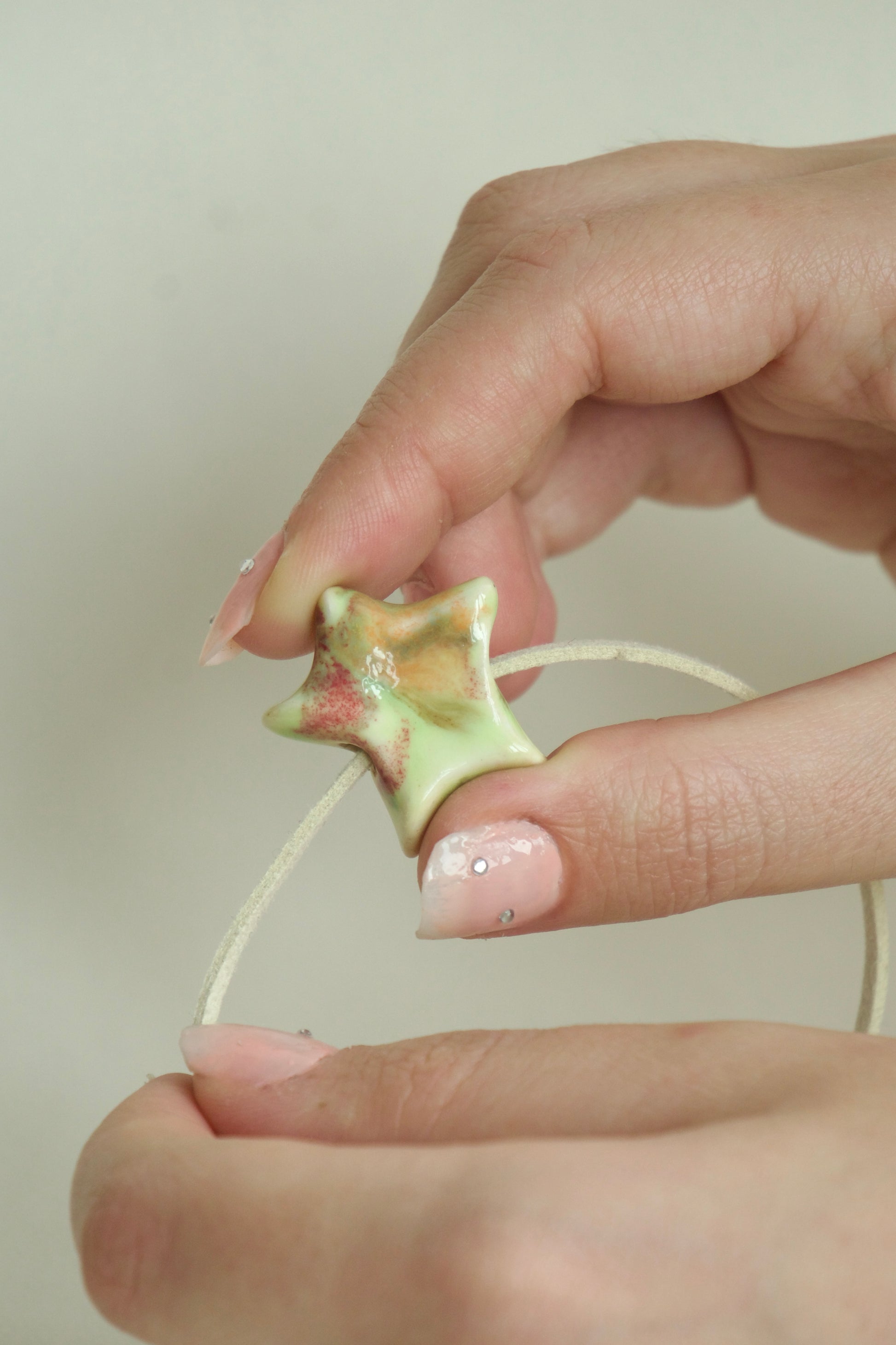 Charm handmade steluță din ceramică, multicolor pastel cu accente roz și verde cu șnur suede bej, prezentat în mână, produs unicat.